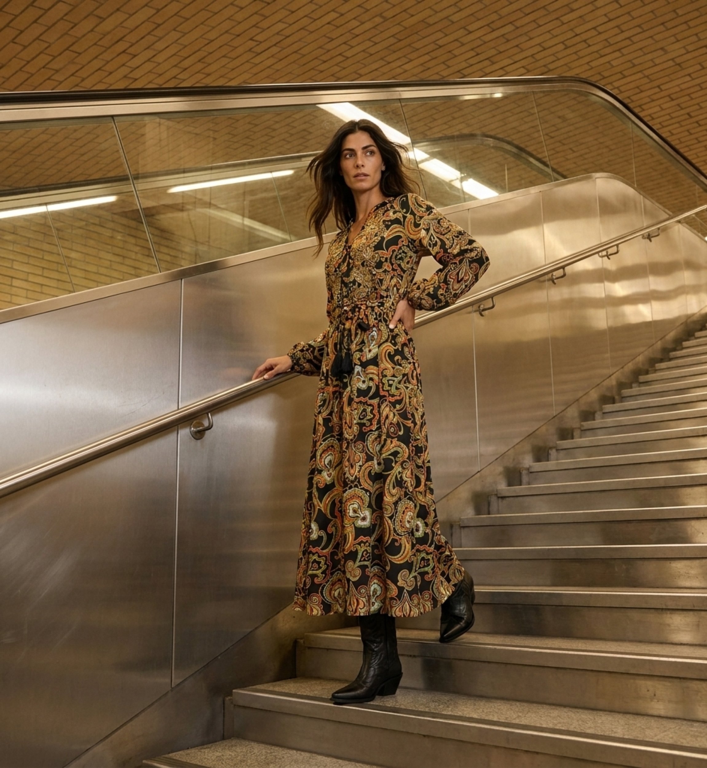 Schwarzes Langarm-Maxikleid mit buntem Paisley-Muster, V-Ausschnitt, Bindegürtel und Quasten, fließender Stoff, auf Stadttreppe.