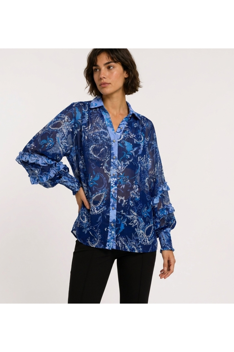 Vista tre quarti di blusa trasparente blu a maniche lunghe con fantasia floreale paisley, polsini a balze e scollo a V.