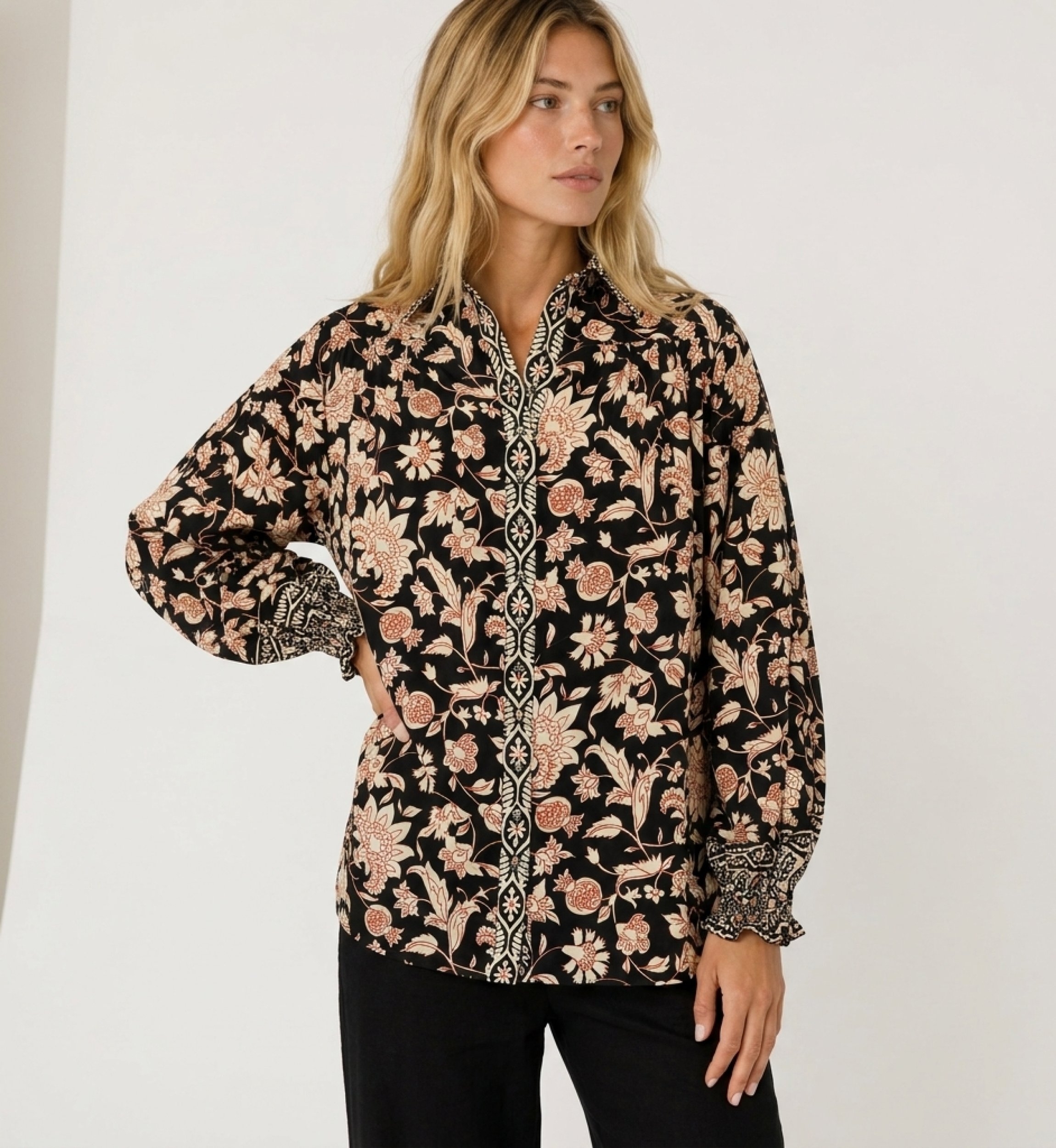 Blusa nera a maniche lunghe con fantasia floreale crema e ruggine, collo e polsini a balze in tessuto leggero.
