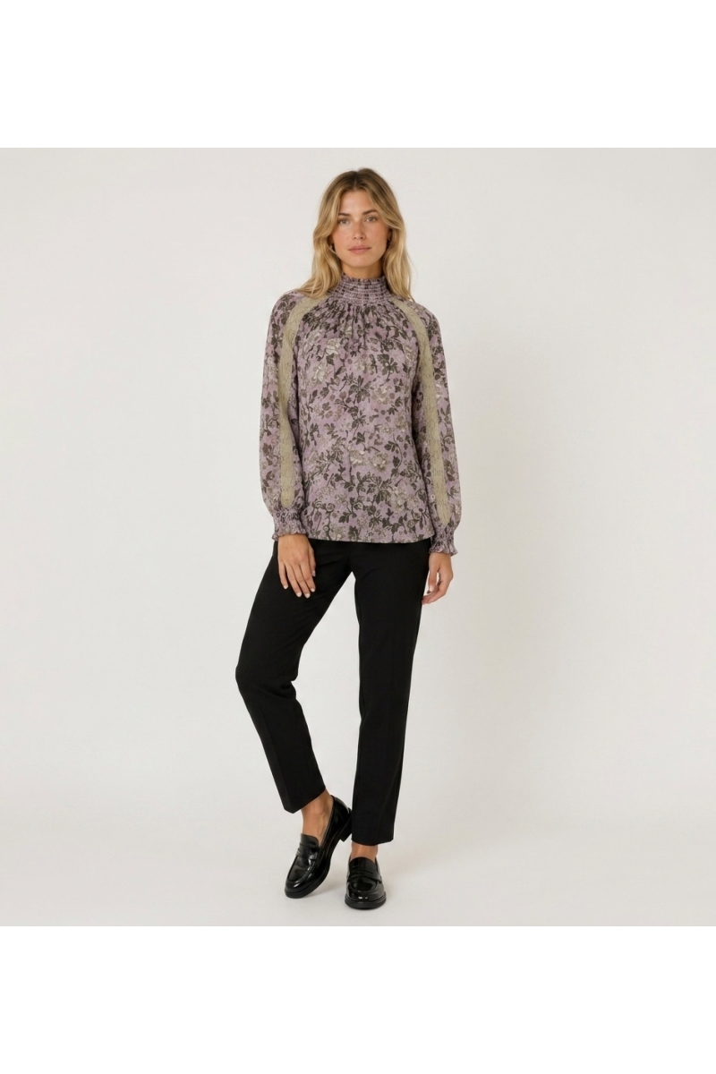 Blusa morada de manga larga y cuello alto con estampado floral oscuro, ribete de encaje beige y puños fruncidos, vista frontal.