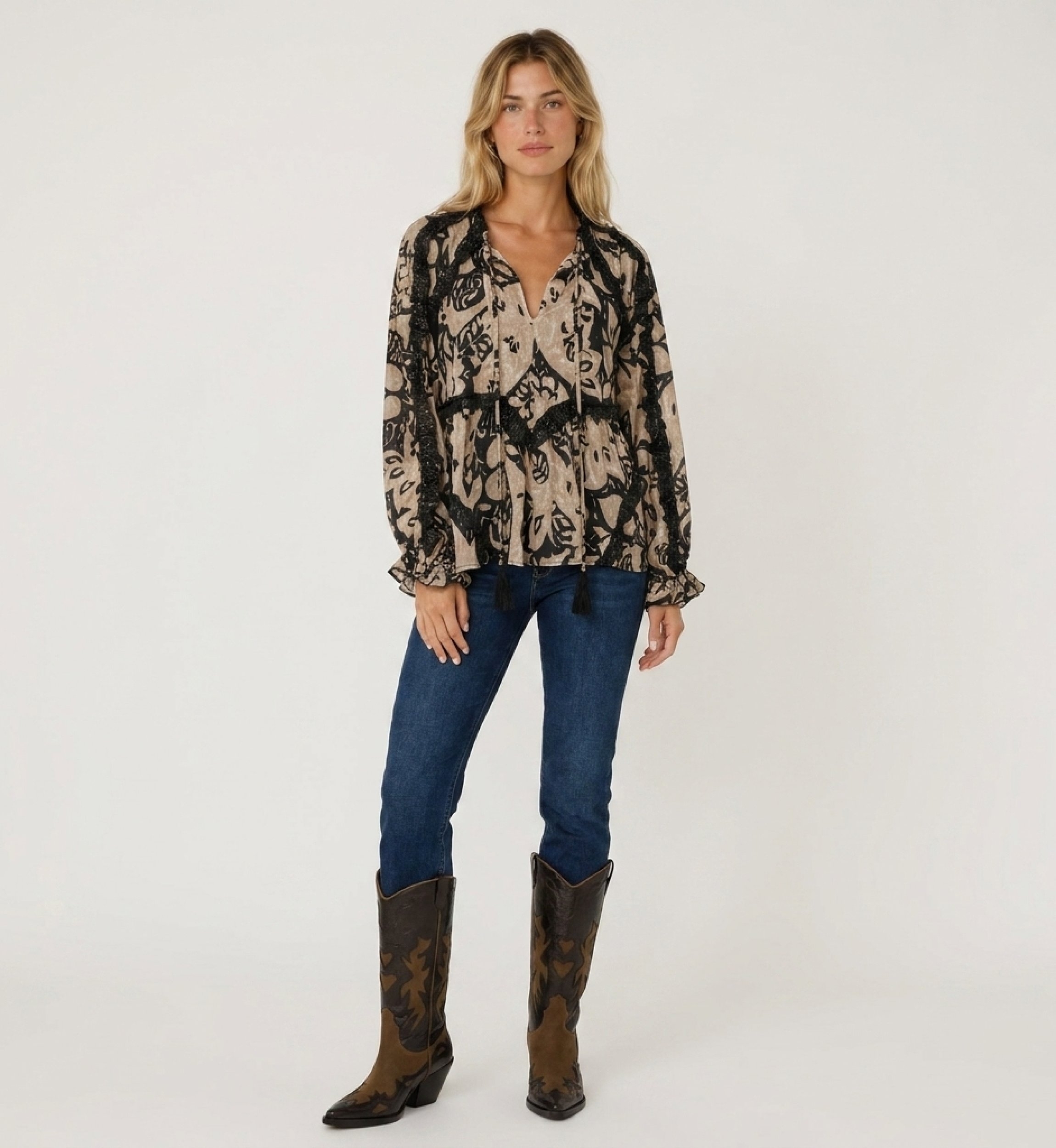 Front view of a loose-fit long-sleeve beige and black patterned blouse with ruffled trim, tassel details, lightweight fabric.