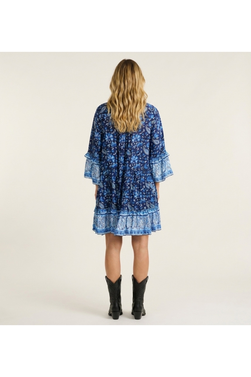 Back view of a blue and white paisley floral mini dress with collared V-neck, three-quarter ruffled sleeves, and tiered skirt.