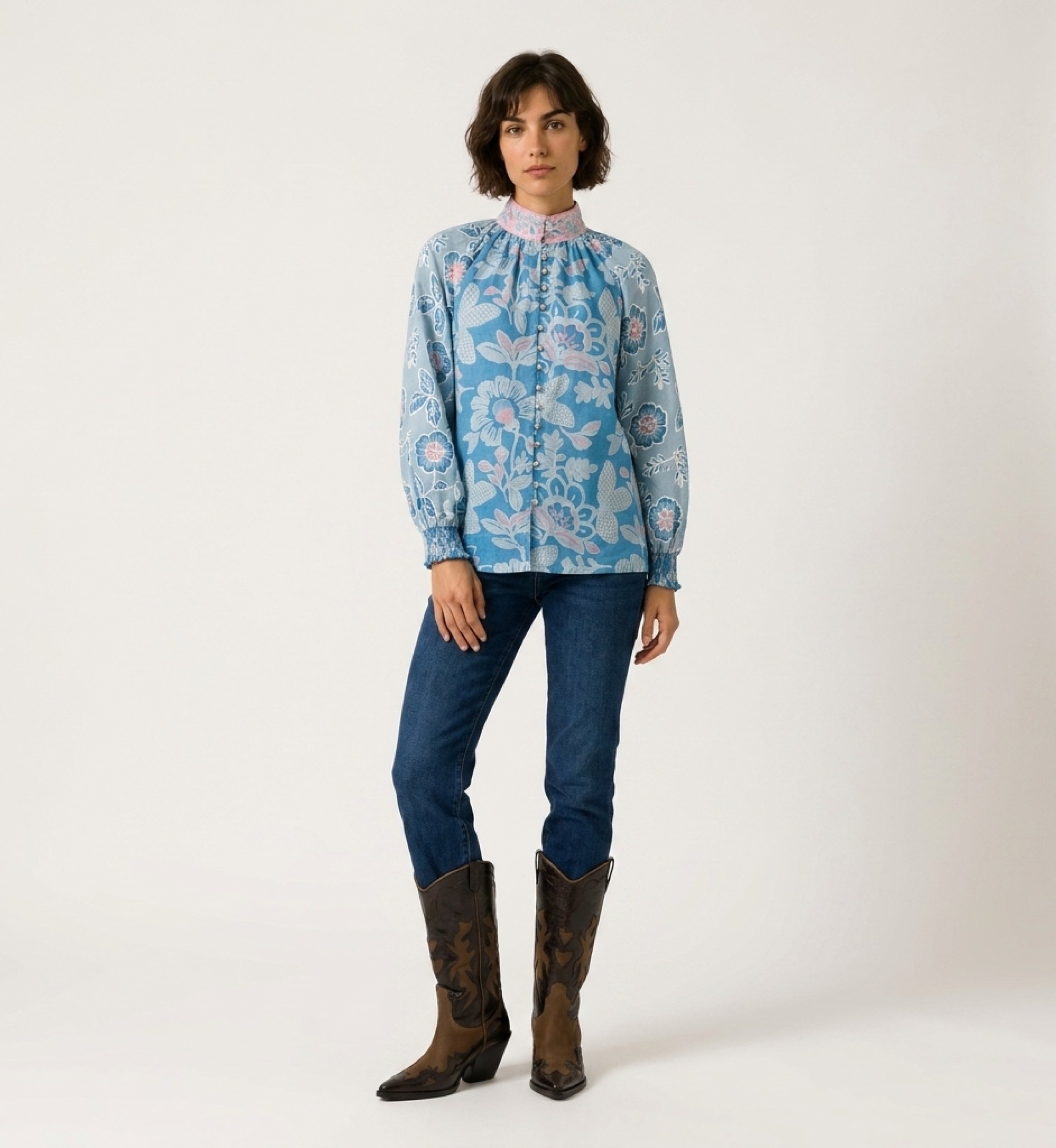 Vue de face d'une blouse bleue à manches longues avec motifs floraux roses et blancs, col haut et coupe ample.