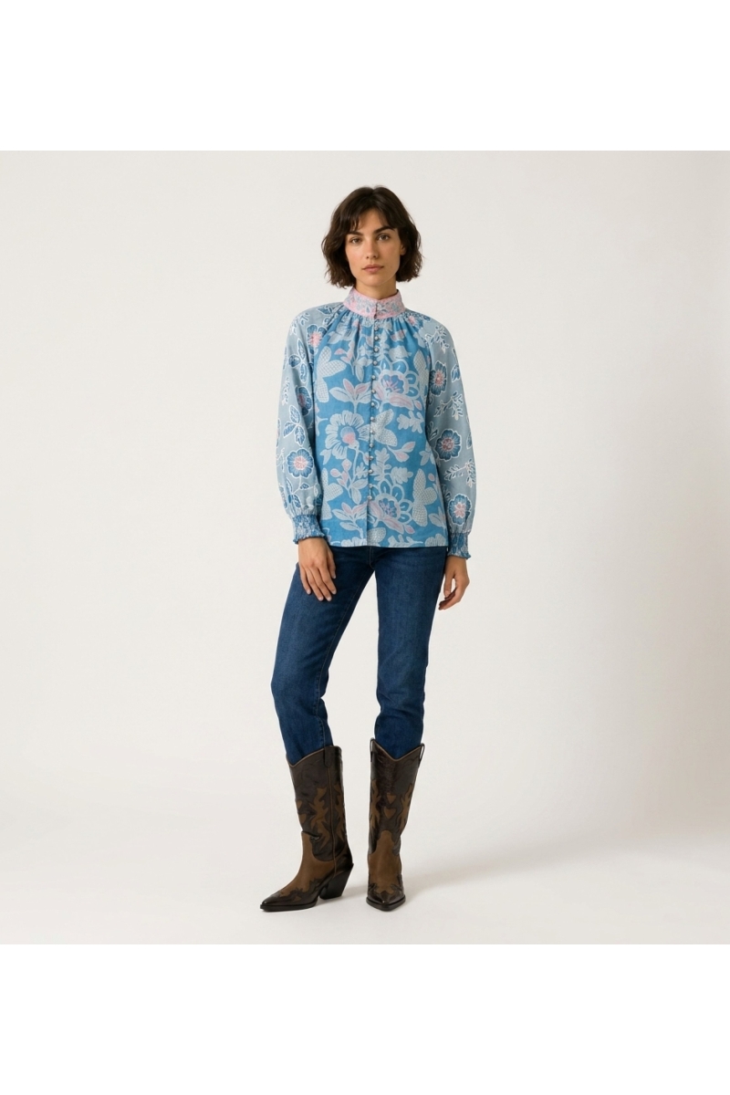 Vista frontale di una blusa blu a maniche lunghe con fantasia floreale rosa e bianca, collo alto, vestibilità ampia.