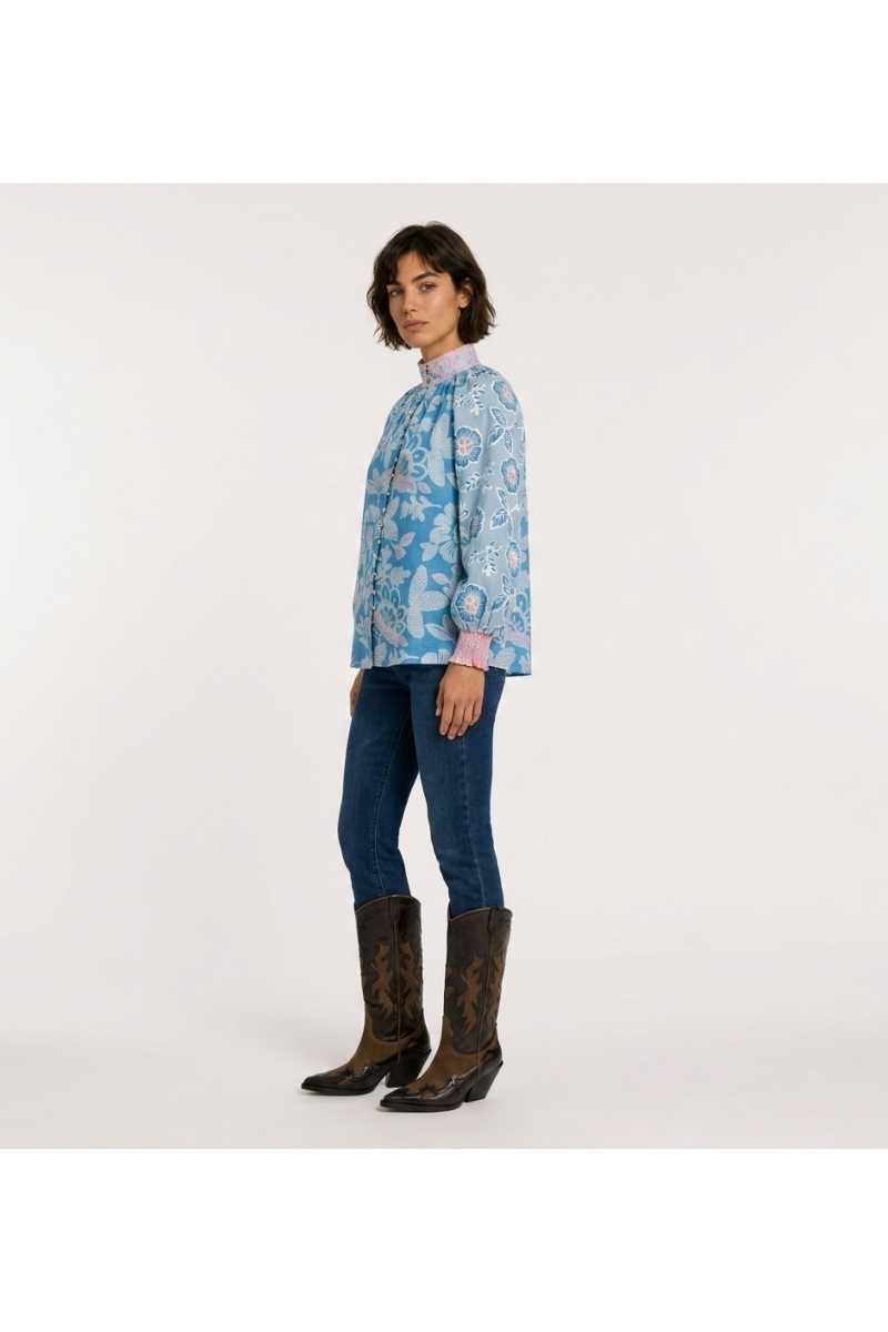 Blusa azul de manga comprida com estampa floral rosa e branca, gola alta, caimento solto, tecido algodão, vista lateral 3/4.