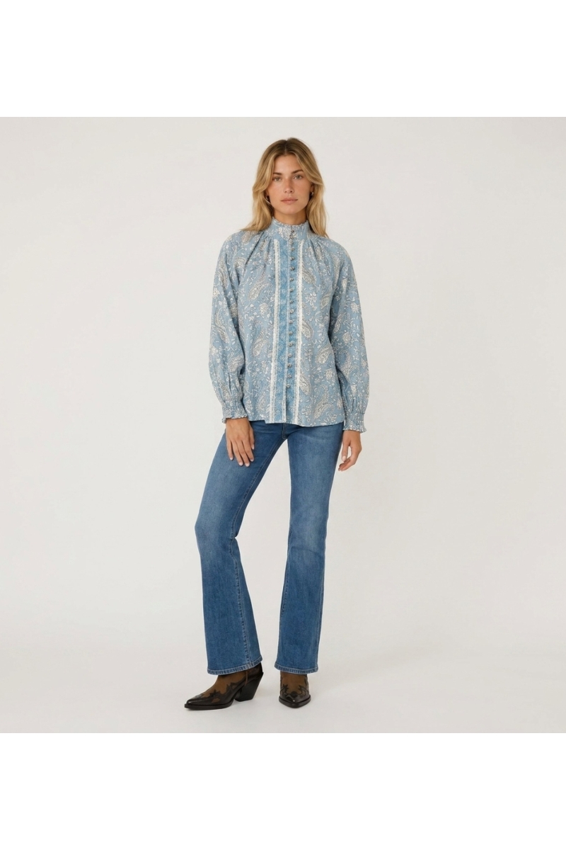 Blusa azzurra a maniche lunghe con fantasia paisley bianca, collo alto, abbottonatura frontale e polsini con volant.