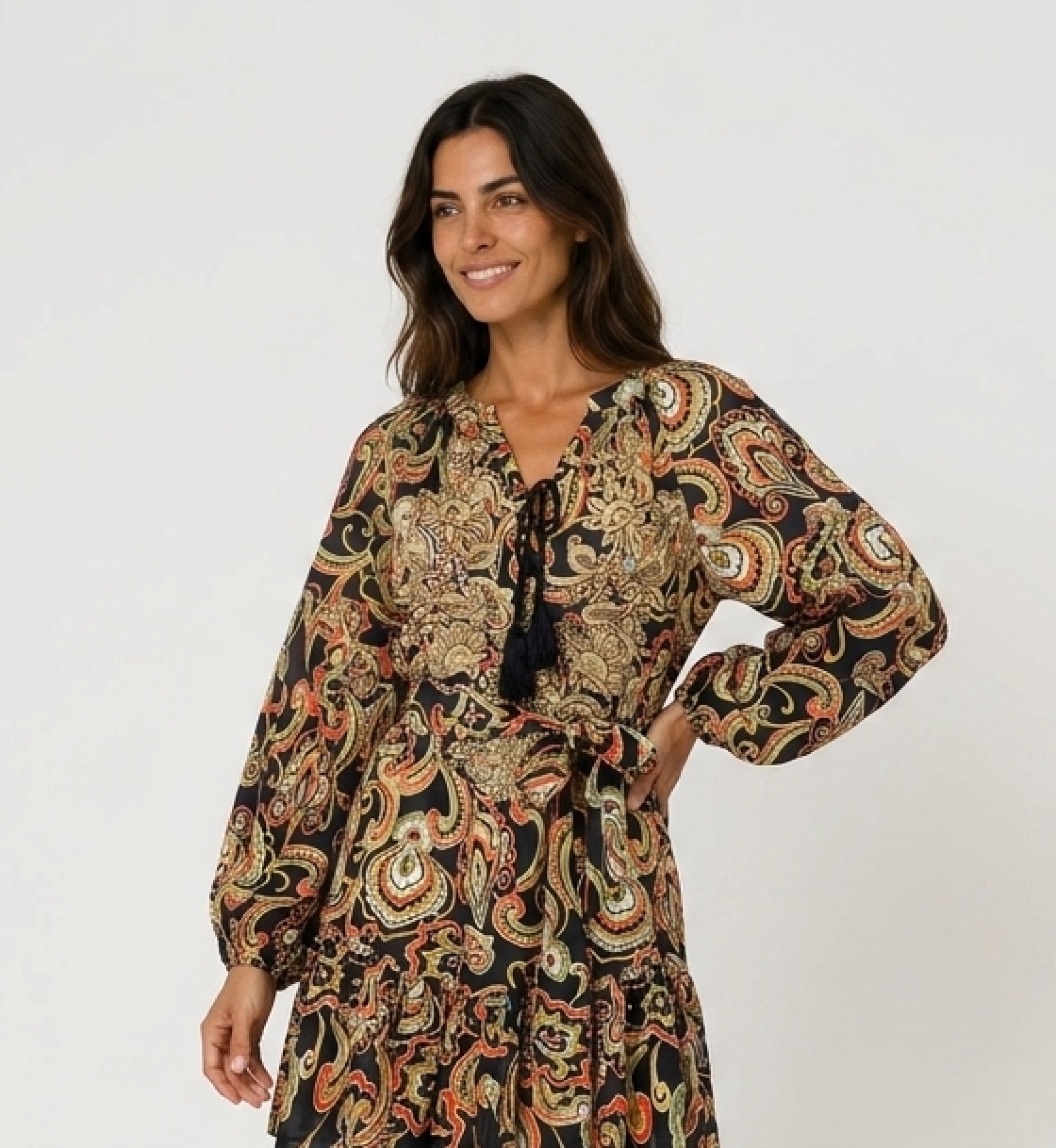 Black long-sleeve mini dress with colorful paisley print, tie-neck & tassels, cinched waist, and ruffled hem.