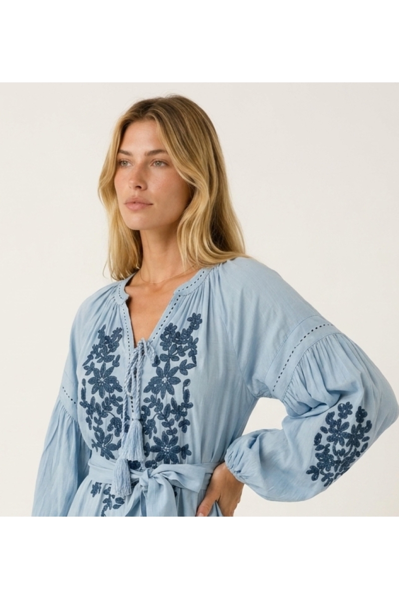 Robe courte noire ample, manches ballon longues, jupe à volants, broderie florale blanche, taille nouée, vue de trois-quarts.