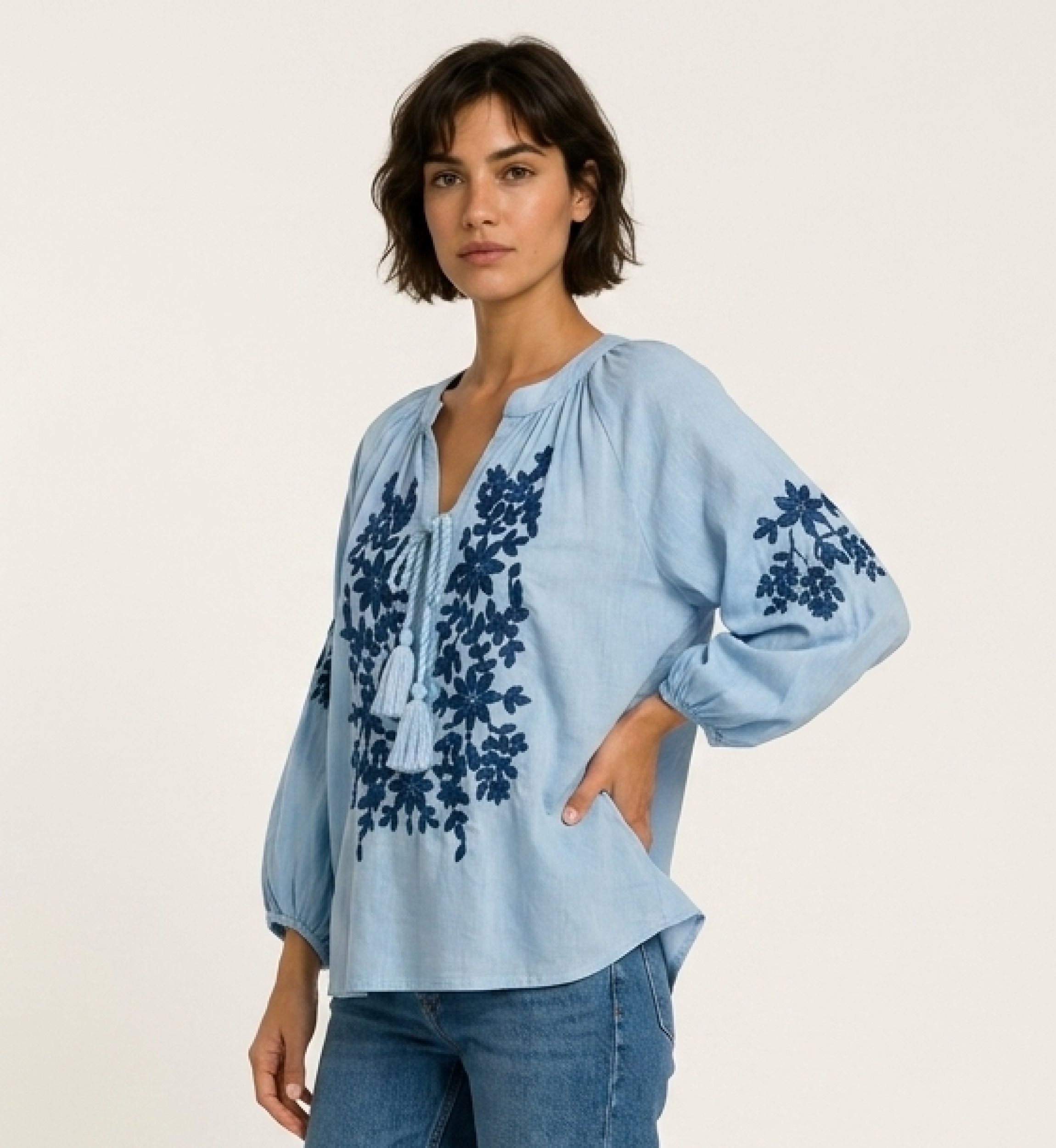 Black long-sleeve peasant blouse with v-neck, tie closure, and cream floral embroidery. Linen-like fabric, three-quarter view.