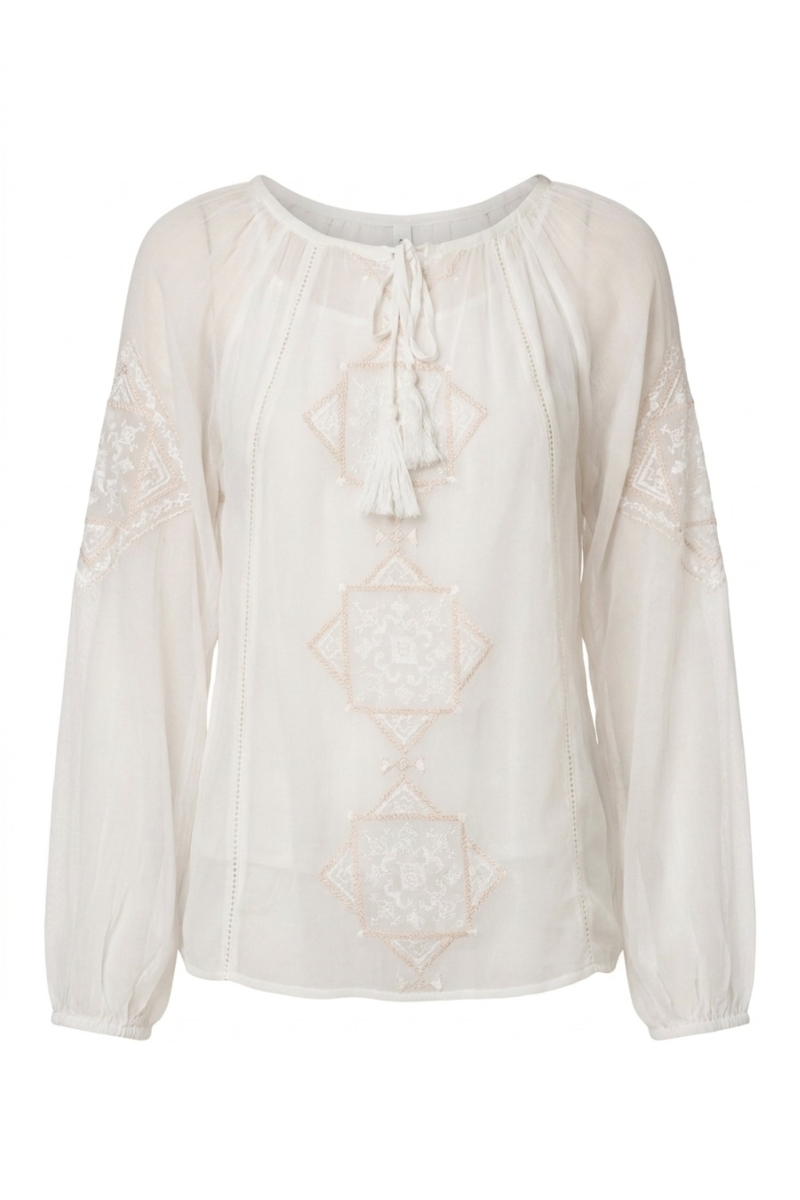 Blouse ample écru manches longues avec col lavallière brodé, portée avec un pantalon noir fluide large.